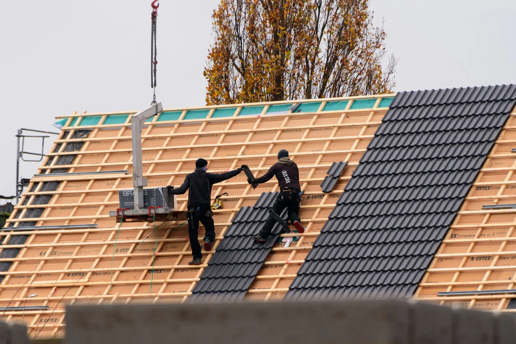 Zwei Dachdecker von hinten verlegen dunkle Ziegel auf neuer Lattung